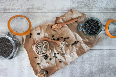 sunflower seeds, flax seeds in glass jars and wooden spoons on a crumpled brown paper backgroundの写真素材