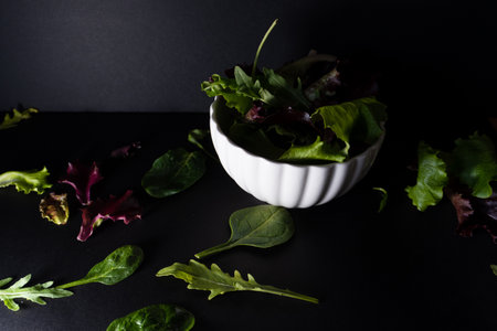 A WHITE BOWL WITH LETTUCE LEAVES OF DIFFERENT TYPES ON A BLACK BACKGROUNDの写真素材