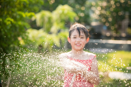Blur background of Asian girl playing with water hose outdoors in the garden at the backyard of the house on a hot sunny summer dayの写真素材