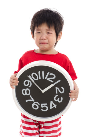 Asian child crying and holding a clock on white background isolatedの写真素材