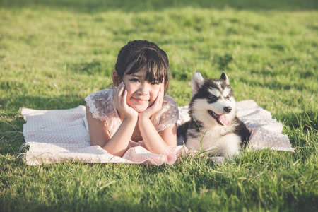 Beautiful asian girl lying on green grass with a siberian husky puppy,Vintage filterの写真素材