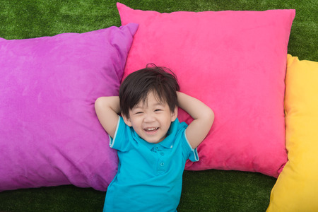 Cute asian child lying with colorful pilows on green grassの写真素材