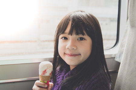 Little asian girl smiling  and eating ice cream.She travels on a train,vintage filterの写真素材