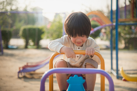 Cute asian child riding seesaw board at the playground under sunlightの写真素材