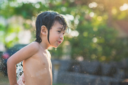 Cute asian boy has fun playing in water from a hose outdoorsの写真素材