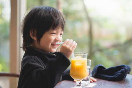 Cute asian child drinking fresh orange juiceの写真素材