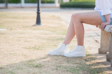 Asian woman in white sneakers  sitting on Stone benchの写真素材