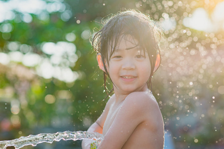 Cute asian boy has fun playing in water from a hose outdoorsの写真素材