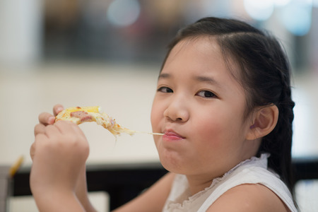 Asian girl eating a piece of pizza in a restaurantの写真素材