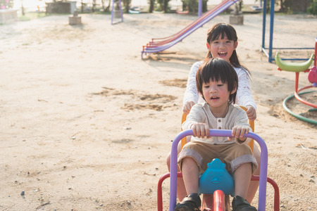 Cute asian children riding seesaw board at the playground under sunlightの写真素材