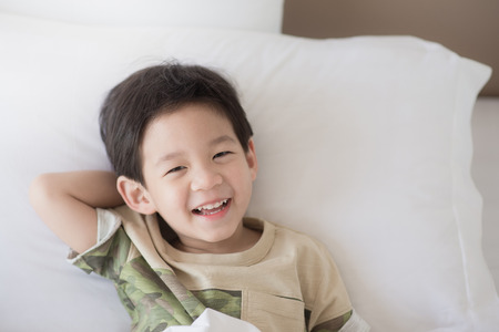 Cute asian child lying on white bedの写真素材
