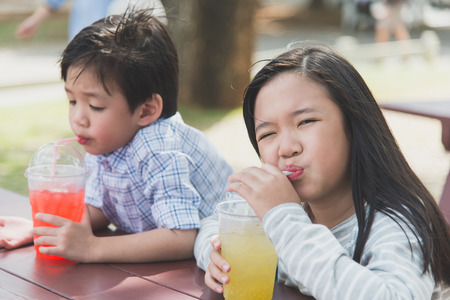 Cute asian children drinking fresh  juice in the park outdoorの写真素材