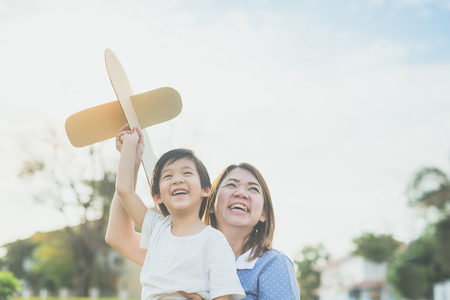 Cute Asian mother and son playing cardboard airplane together in the park outdoorsの写真素材