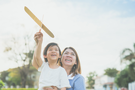 Cute Asian mother and son playing cardboard airplane together in the park outdoorsの写真素材