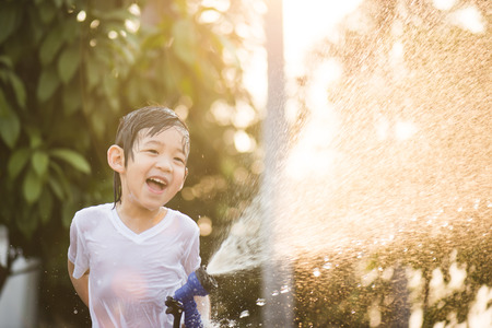 Cute asian boy has fun playing in water from a hose outdoorsの写真素材