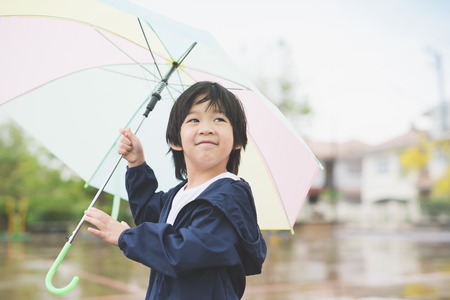 Happy asian boy holding colorful umbrella playing in the park after the rainの写真素材