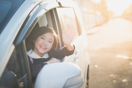 Asian girl in student uniform going to school by car and  waving goodbyeの写真素材