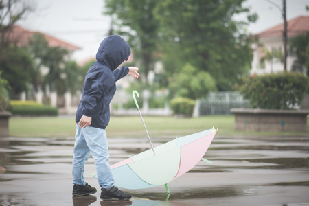 Happy asian boy holding colorful umbrella playing in the park after the rainの写真素材