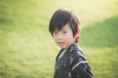 Portrait of cute Asian boy in kimono with green field backgroundの写真素材