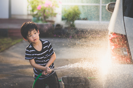 Cute asian child washing a car with hose on summer dayの写真素材
