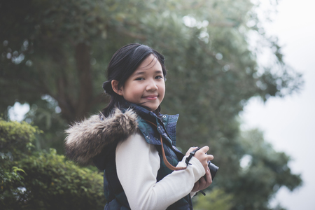 Beautiful Asian girl  in warm clothes with retro  camera shooting a photo in the parkの写真素材