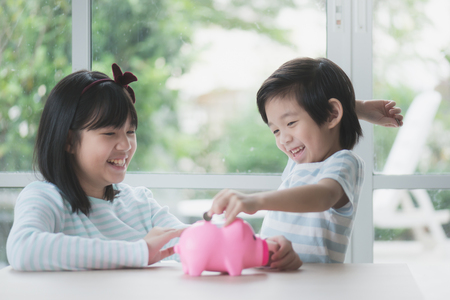 Cute Asian child putting a coin into a piggy bankの写真素材