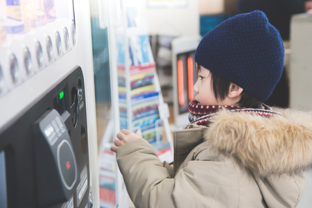 Cute Asian child purchasing soft drink from vending machine in the train stationの写真素材