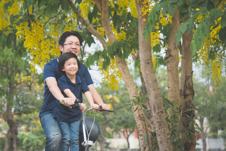 Happy Asian  father and son riding bicycle together with spring backgroundの写真素材