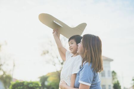 Cute Asian mother and son playing cardboard airplane together in the park outdoorsの写真素材