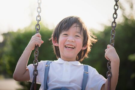 Cute Asian child having fun on swing in the parkの写真素材