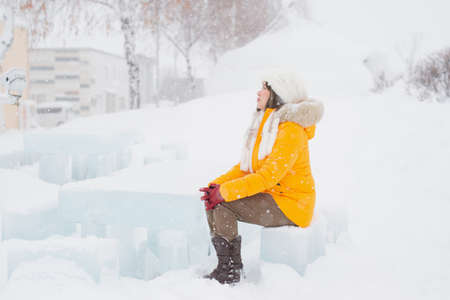 Asian woman wearing yellow clothes sitting on ice chair in snowfall
