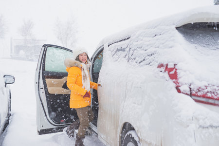 Asian woman wearing yellow clothes getting in to a van under snowfallの写真素材