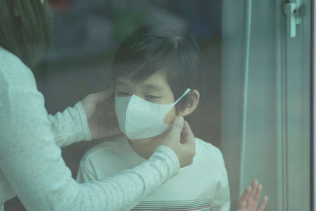 Asian mother puts a safety mask on her son's face while stay isolation at homeの写真素材