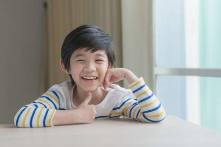 Cute Asian child resting chins on hands on wood tableの写真素材