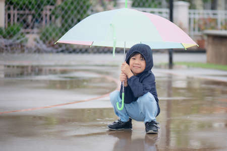 Happy asian boy holding colorful umbrella playing in the park after the rainの写真素材