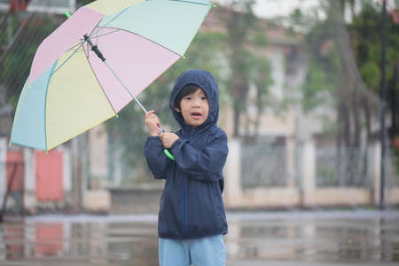 Happy asian boy holding colorful umbrella playing in the park after the rainの写真素材