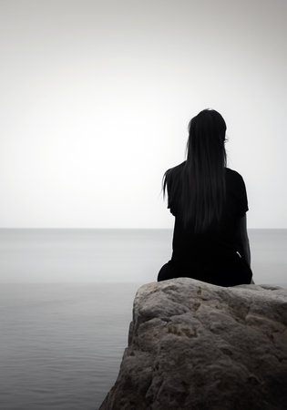 silhouette of a young woman sitting on a rock by the sea