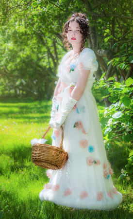 Beautiful girl in an historical bride dress with a wicker basket in her hands in a spring garden for...