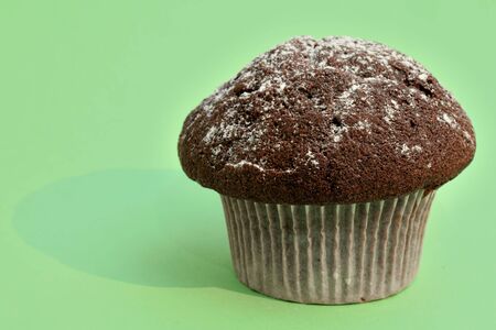 Chocolate muffin decorated with powdered sugar close-up on a green background.の写真素材