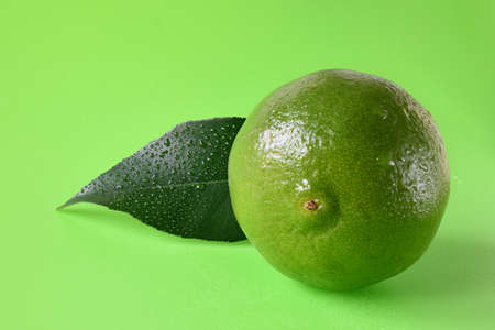 Fresh lime with leaf on a green background.