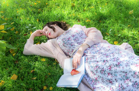 A girl with a book fell sleep in the park on grass on a warm autumn day.の写真素材