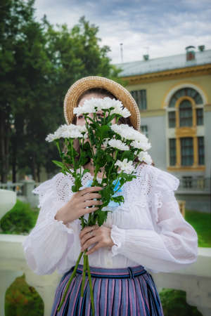 Portrait girl with a bouquet of white chrysanthemums in an vintage shirt and a long skirt on terrace...