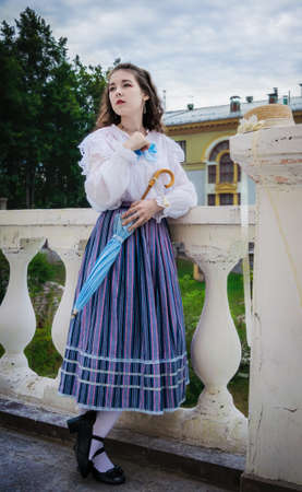 Woman in a vintage shirt and a long skirt with an umbrella on terrace of mansionの写真素材