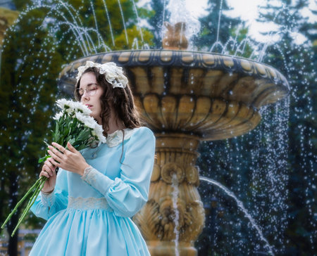 Portrait woman with a bouquet of white chrysanthemums in an elegant vintage dress stands by the fountainの写真素材
