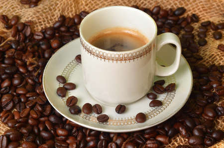 White cup of coffee on coffee beans in the background.