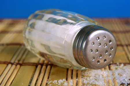 Close up of one salt shaker and salt grain in foreground.