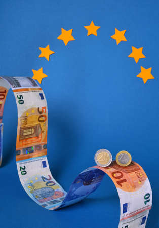 Close up of two Euros coins on a top of a background of Euros banknotes shaped like a roller coaster.の写真素材