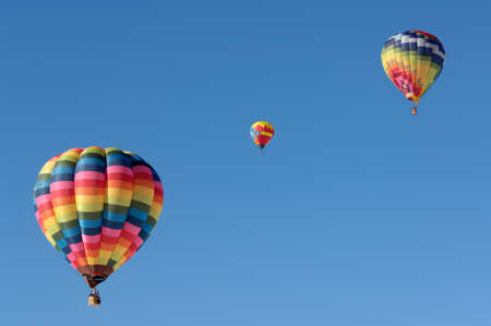 Three multicolored hot air balloons suspended in the blue sky.の写真素材