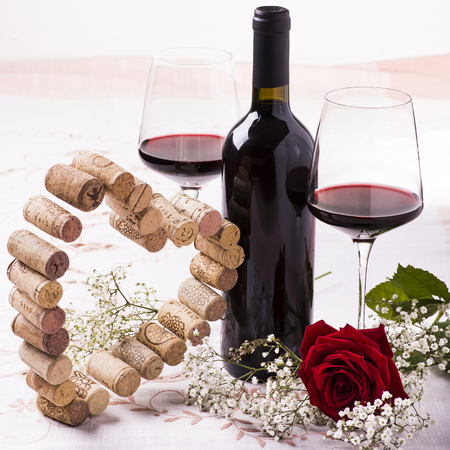 romantic dinner with red wine, floral decoration and silhouette of a heart built with corksの写真素材