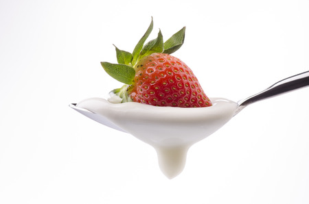 a spoon filled with yogurt with a whole red strawberry on top on a white backgroundの写真素材